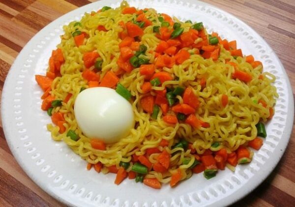 indomie and egg served with vegetables and 2 eggs